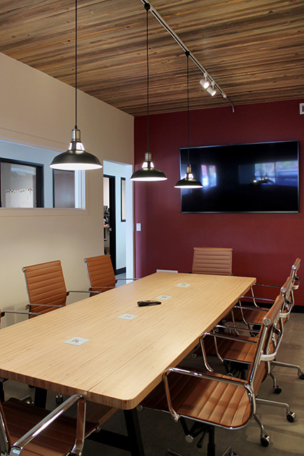 The conference room showing the barn-door-red accent wall, large screen, and exposed wood plank ceiling 